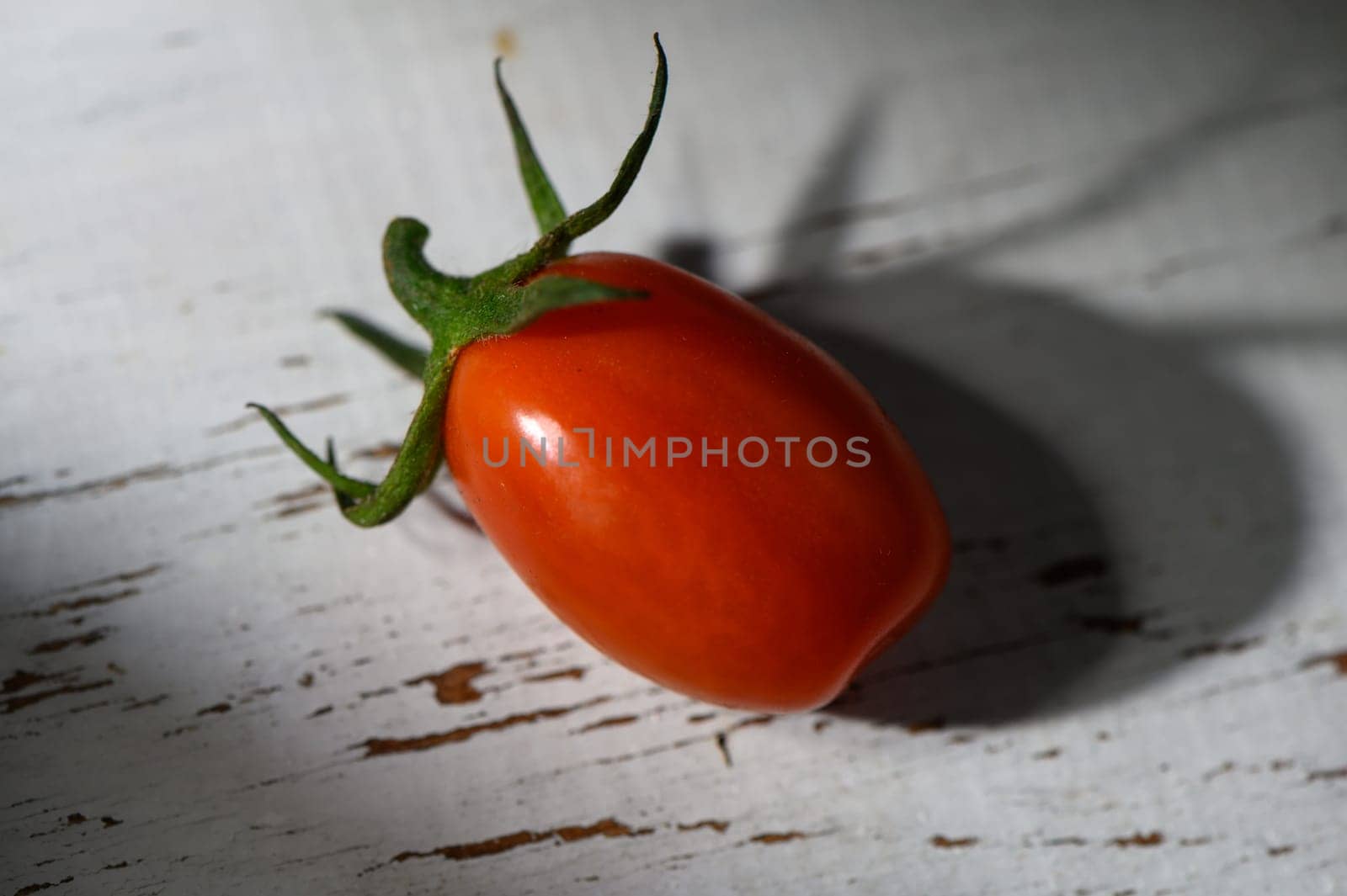 Bright red tomato lies on a weathered wooden surface, highlighting its fresh appearance and organic charm in soft light.