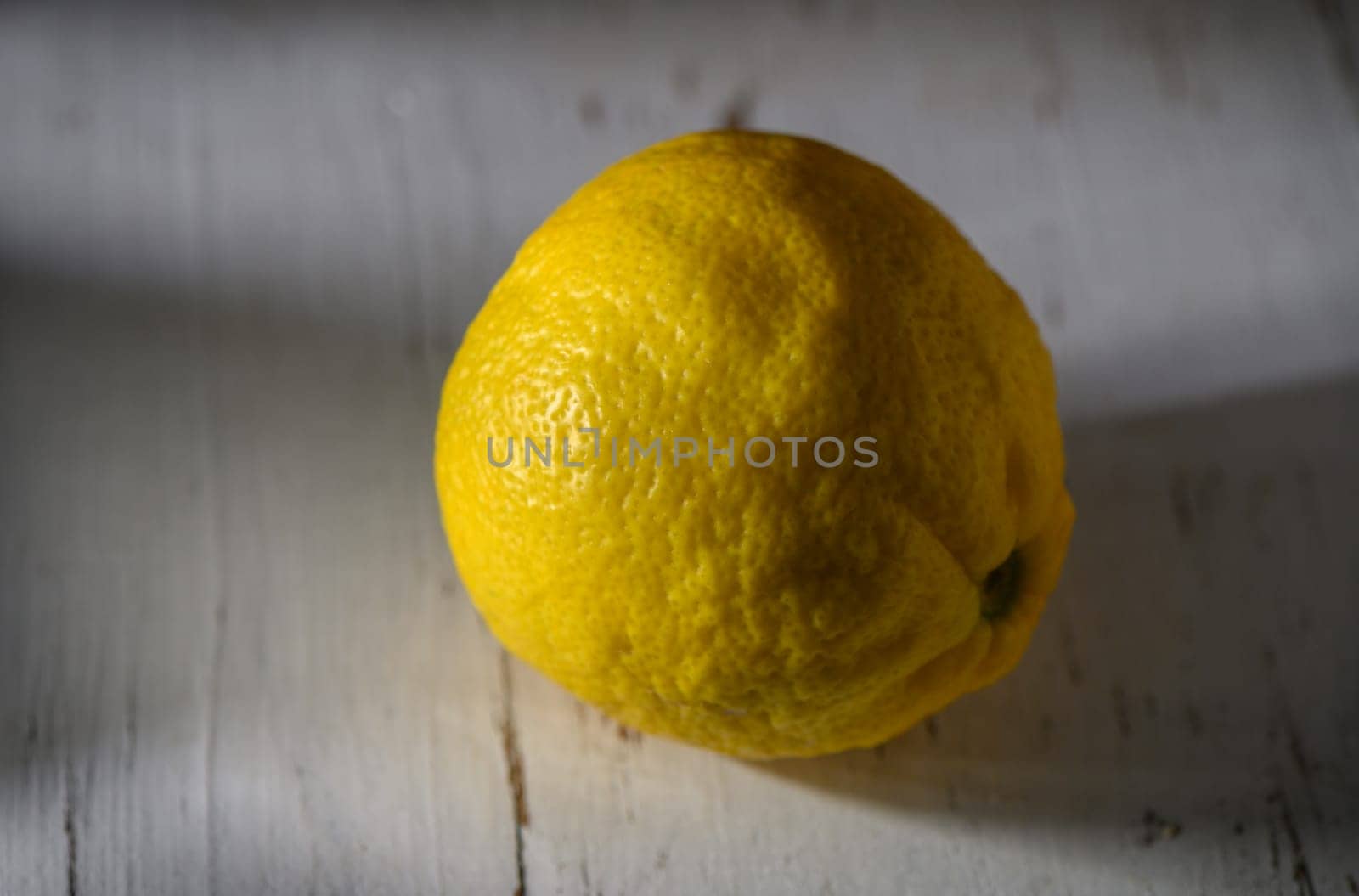 A vibrant lemon sits alone on a weathered table, basking in gentle light that highlights its textured skin.