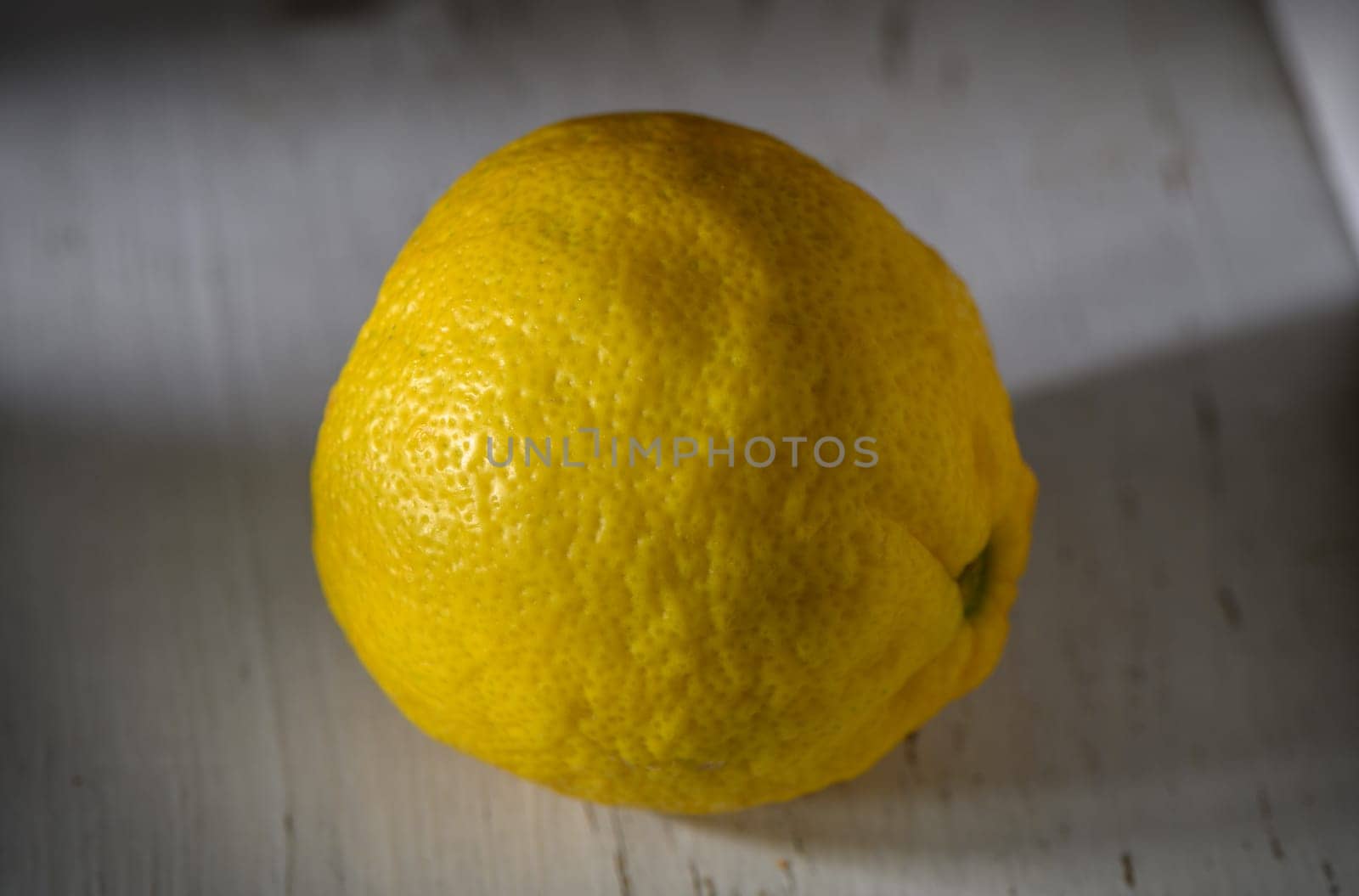 A vibrant lemon sits invitingly on a weathered wooden table, showcasing its fresh, zesty texture and color.