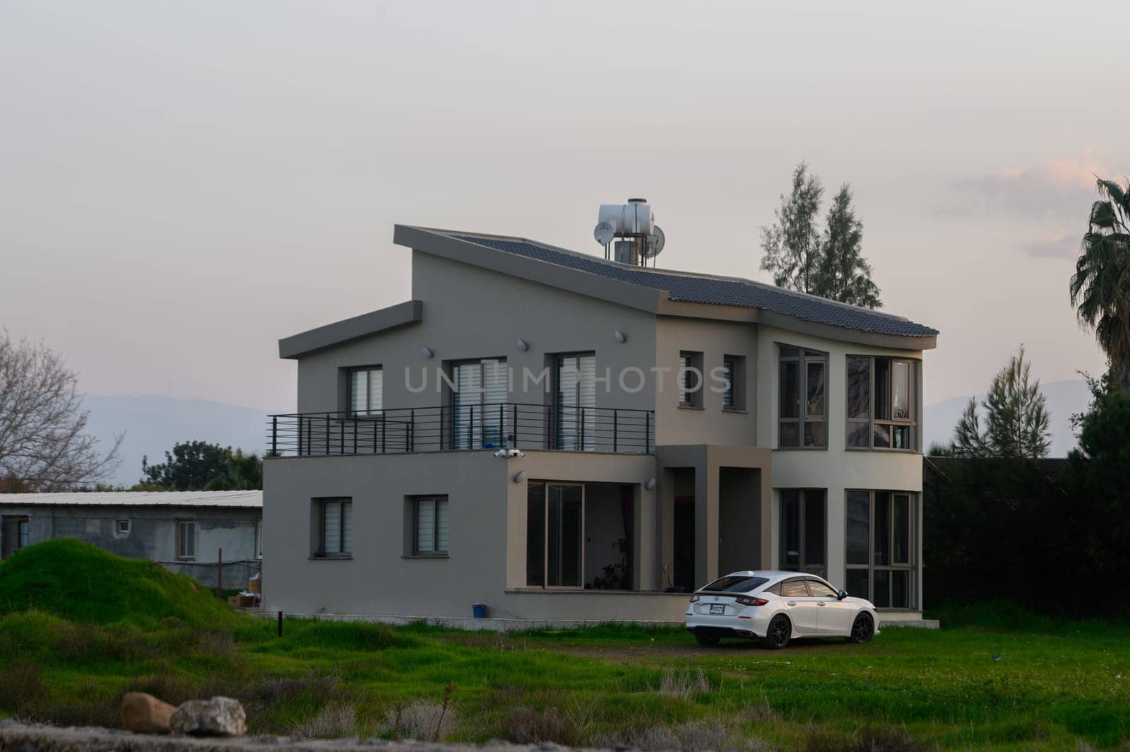 Elegant dwelling stands amidst greenery, overlooking the water as dusk casts soft colors across the sky.