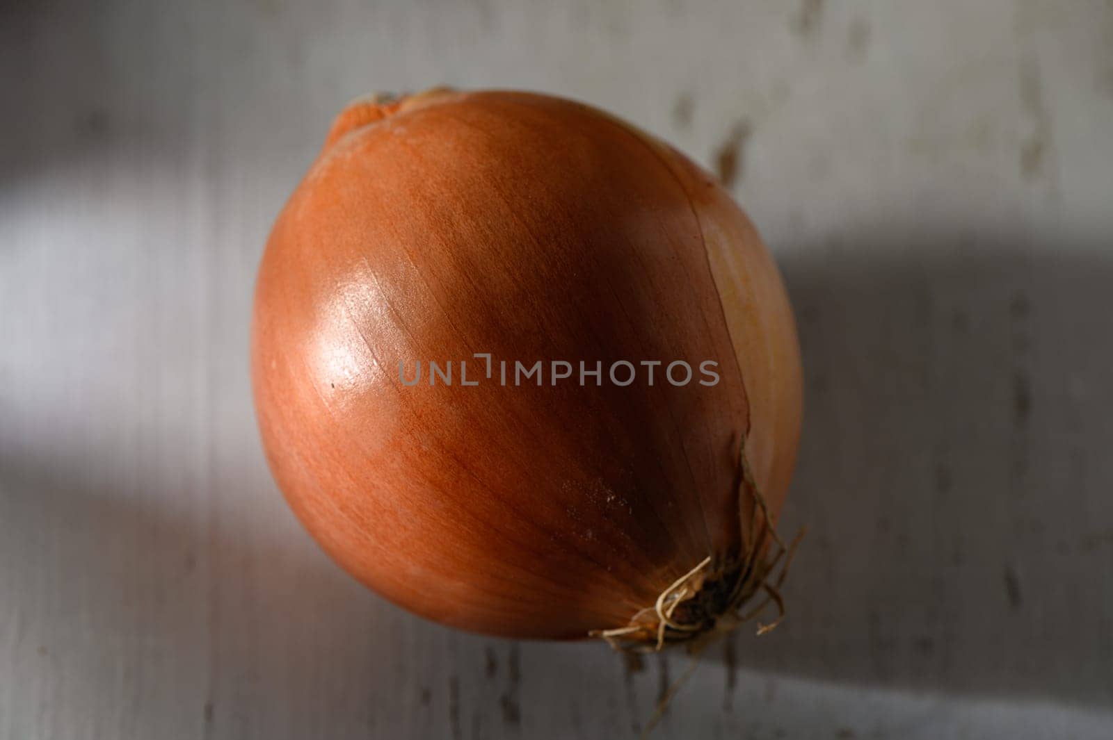 Sunlight shines on a plump onion on a rustic wooden table, highlighting its rich, earthy tones.