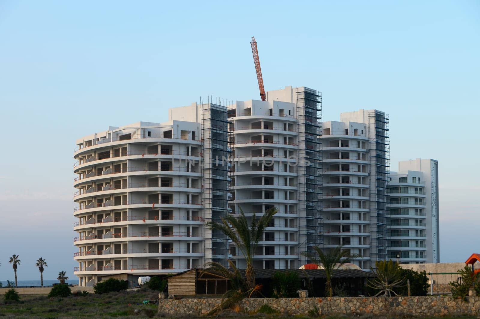 Construction workers busy finishing a sleek coastal high-rise as the sun sets behind the horizon, casting a warm glow.
