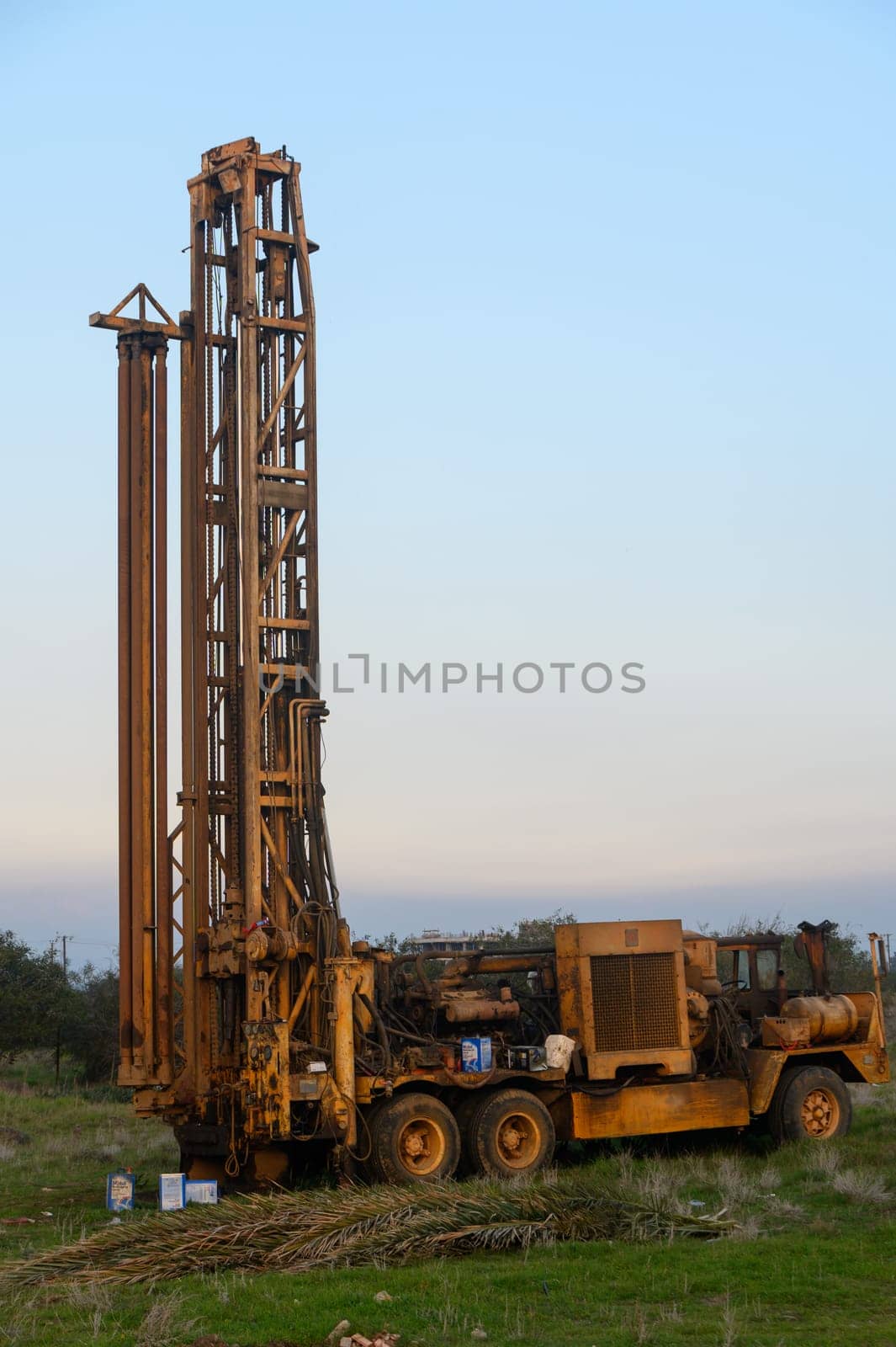 An old drilling rig operates quietly in a peaceful countryside, surrounded by green fields and early morning sunlight.