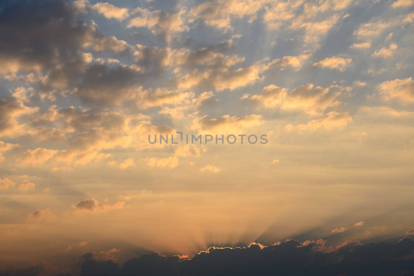 Brilliant hues of orange and gold fill the sky as sunlight streams through fluffy clouds during a serene evening.