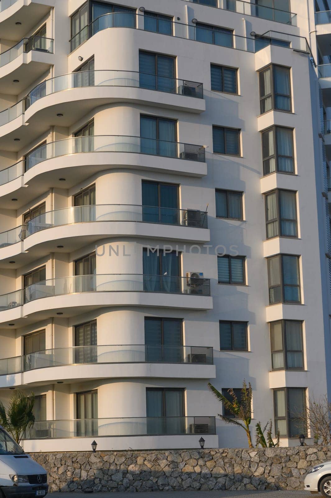 Curved balconies reflect warm sunlight on a contemporary building in a vibrant coastal area at dusk.