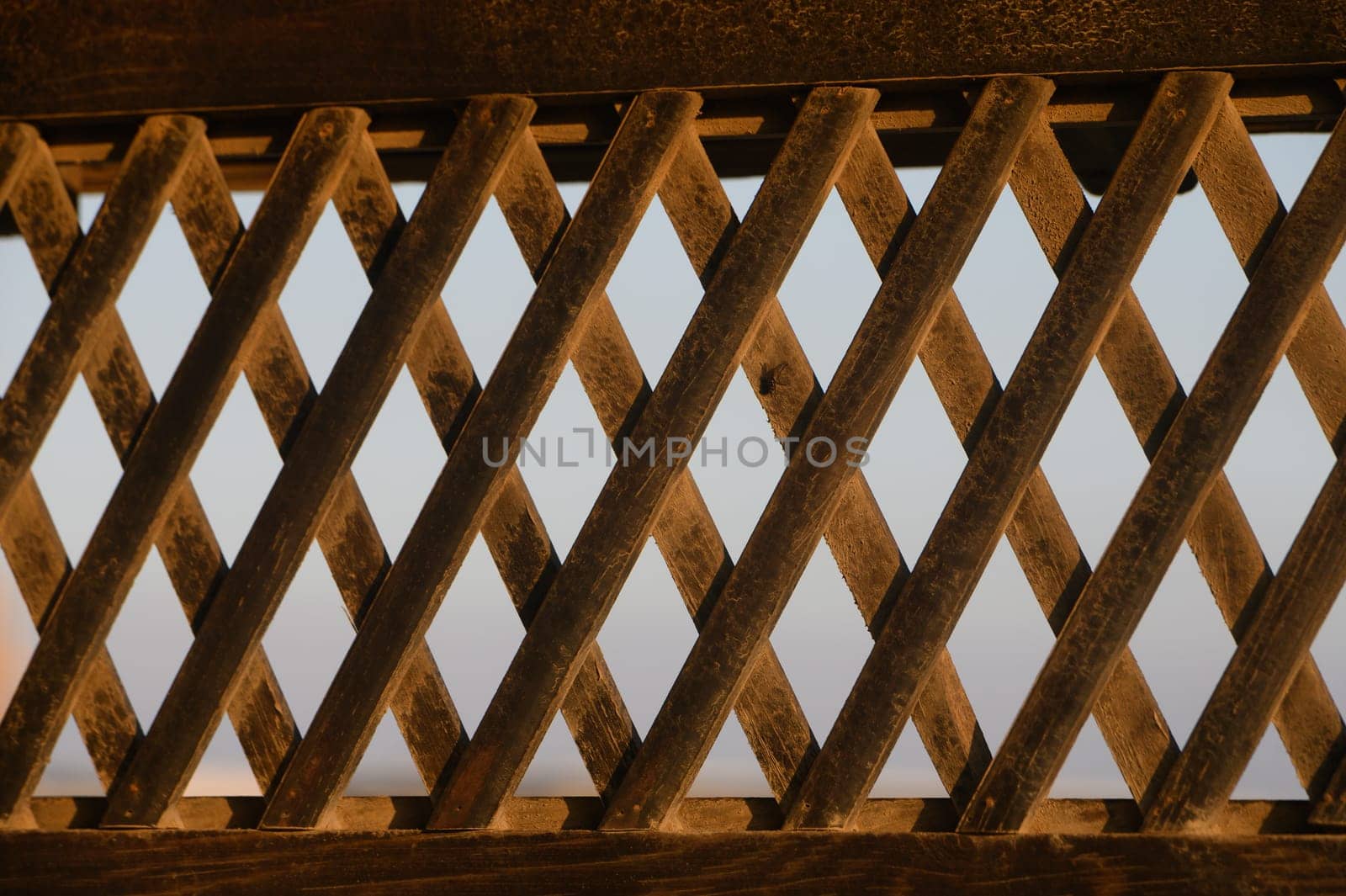 Golden hues illuminate intricate patterns of a wooden lattice during the tranquil evening hours.
