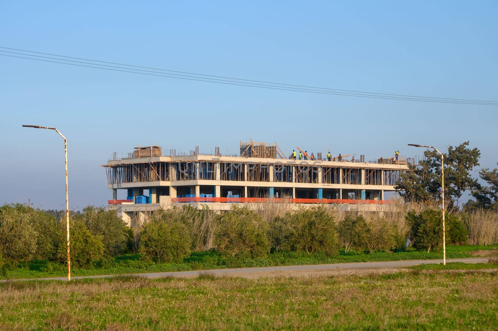 Workers are busy at a construction site for a new building surrounded by greenery and an open sky.