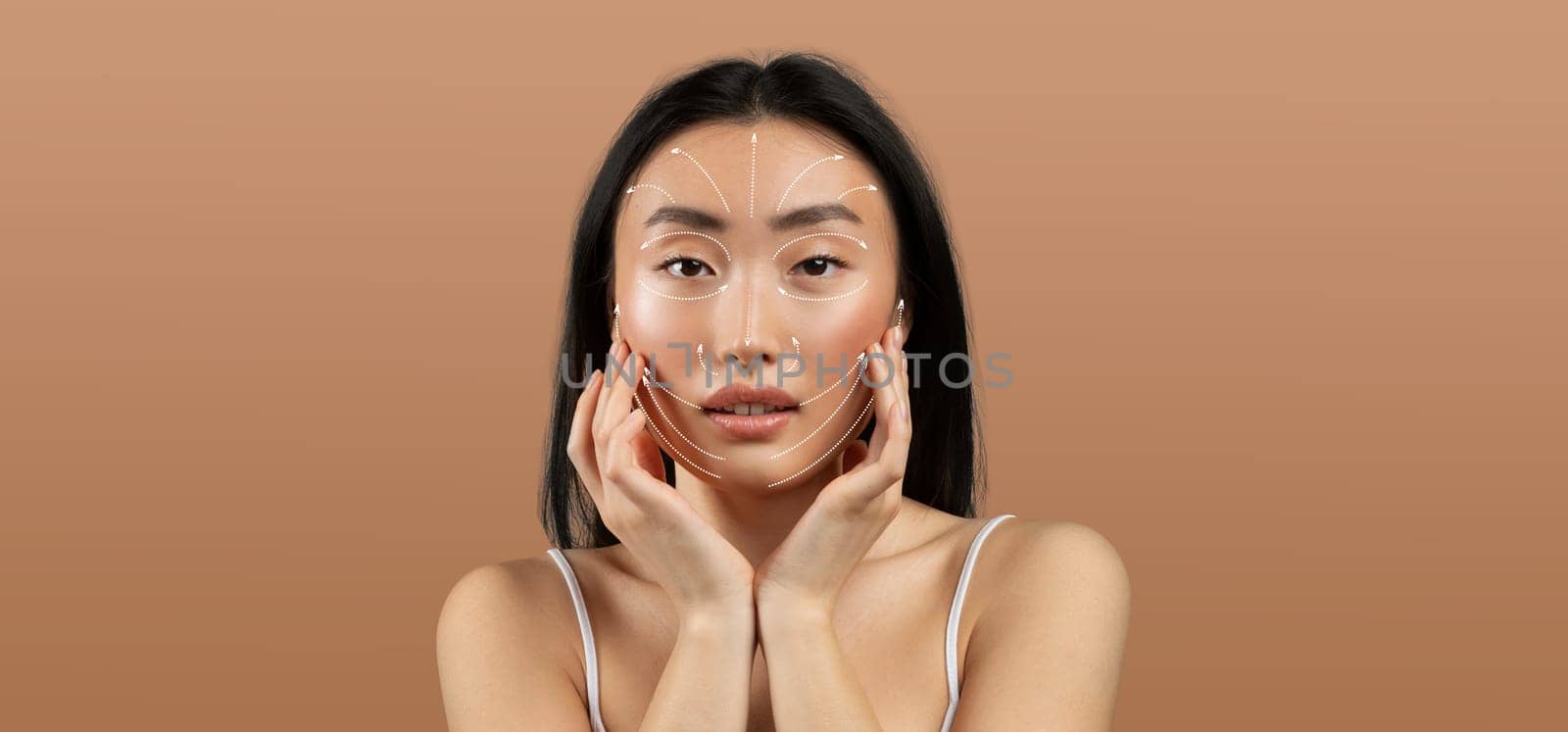 Asian woman practices her skincare routine, gently touching her face. She appears relaxed and focused, surrounded by an empty, neutral backdrop that emphasizes her beauty and self-care.