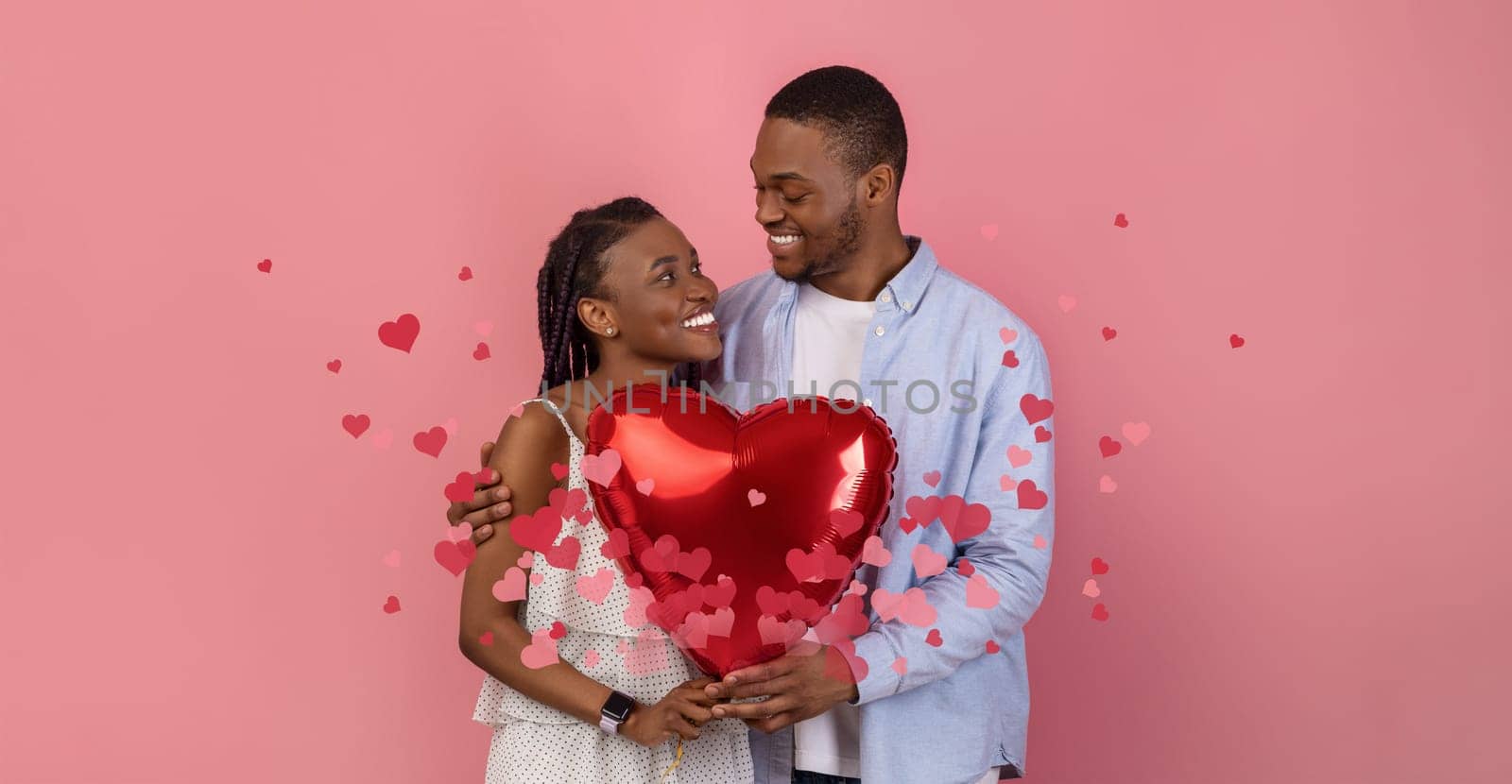 Black couple joyfully celebrates their love, sharing a kiss while holding a large red heart balloon. They are surrounded by floating hearts, symbolizing their bond and affection.