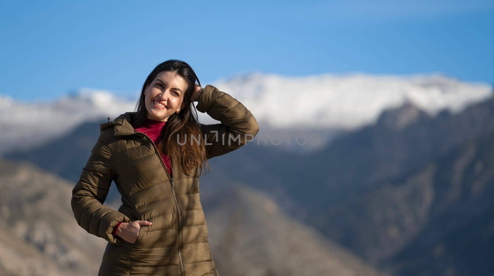 Happy tourist touching her hair while enjoying a beautiful snowy mountain view on a sunny winter day