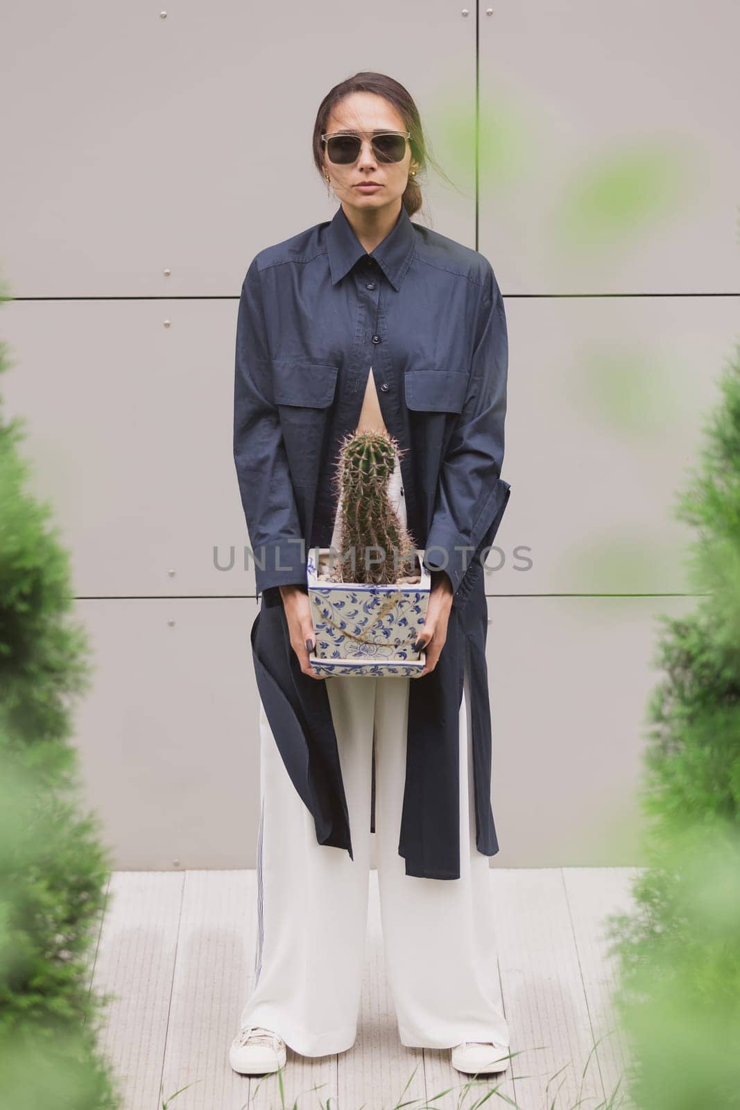 Woman tenderly standing in kimono with cactus in her hands on gray background. The girl seductively wear her robe. Fashionable details of kimono on grey background