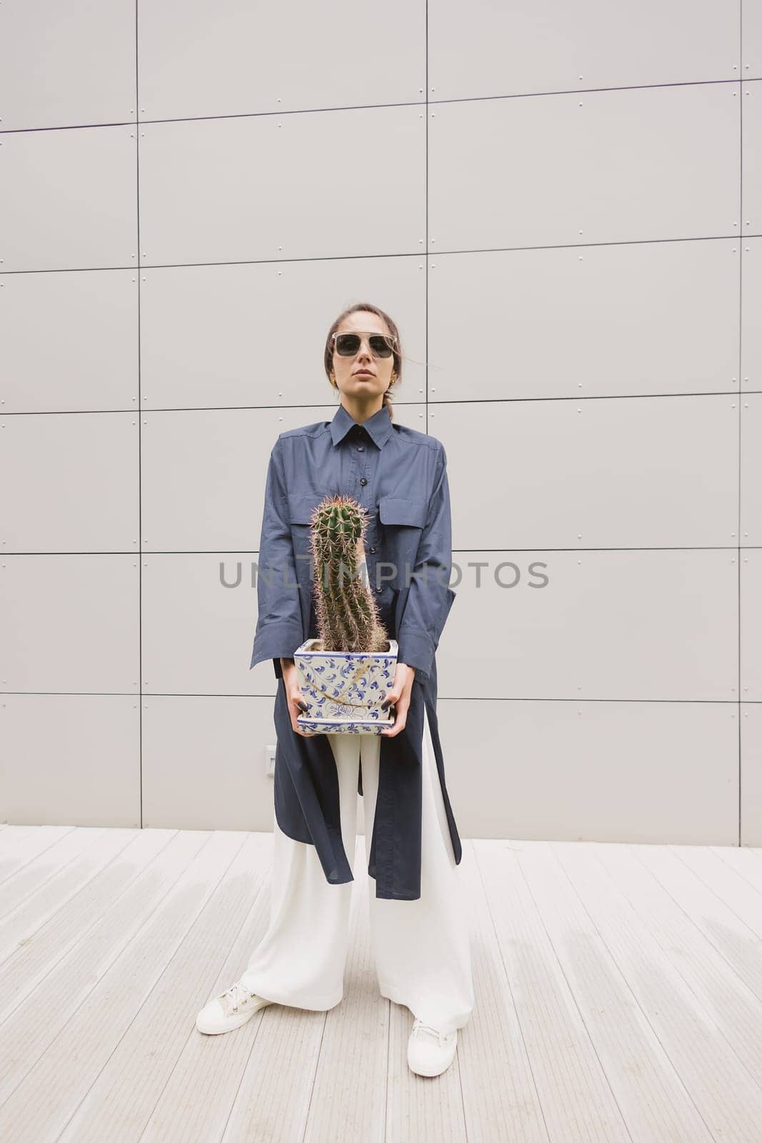 Woman tenderly standing in kimono with cactus in her hands on gray background. The girl seductively wear her robe. Fashionable details of kimono on grey background