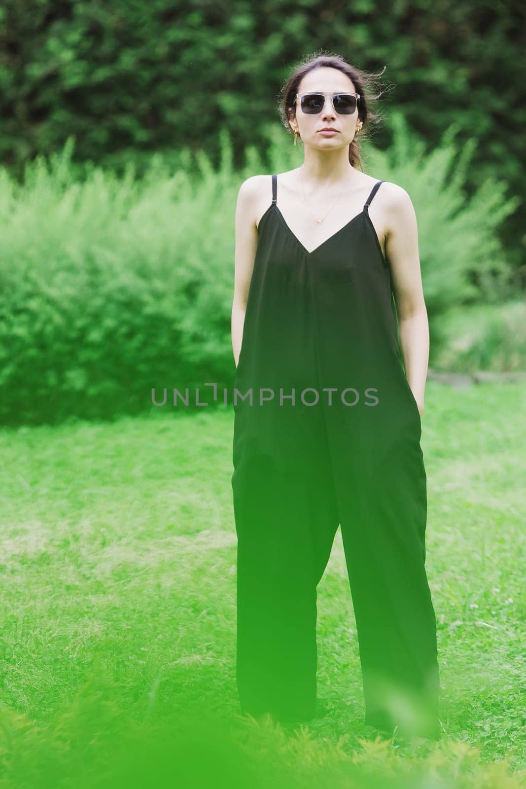 Beautiful young brunette woman, wearing black jumpsuit posing outdoors by sarymsakov