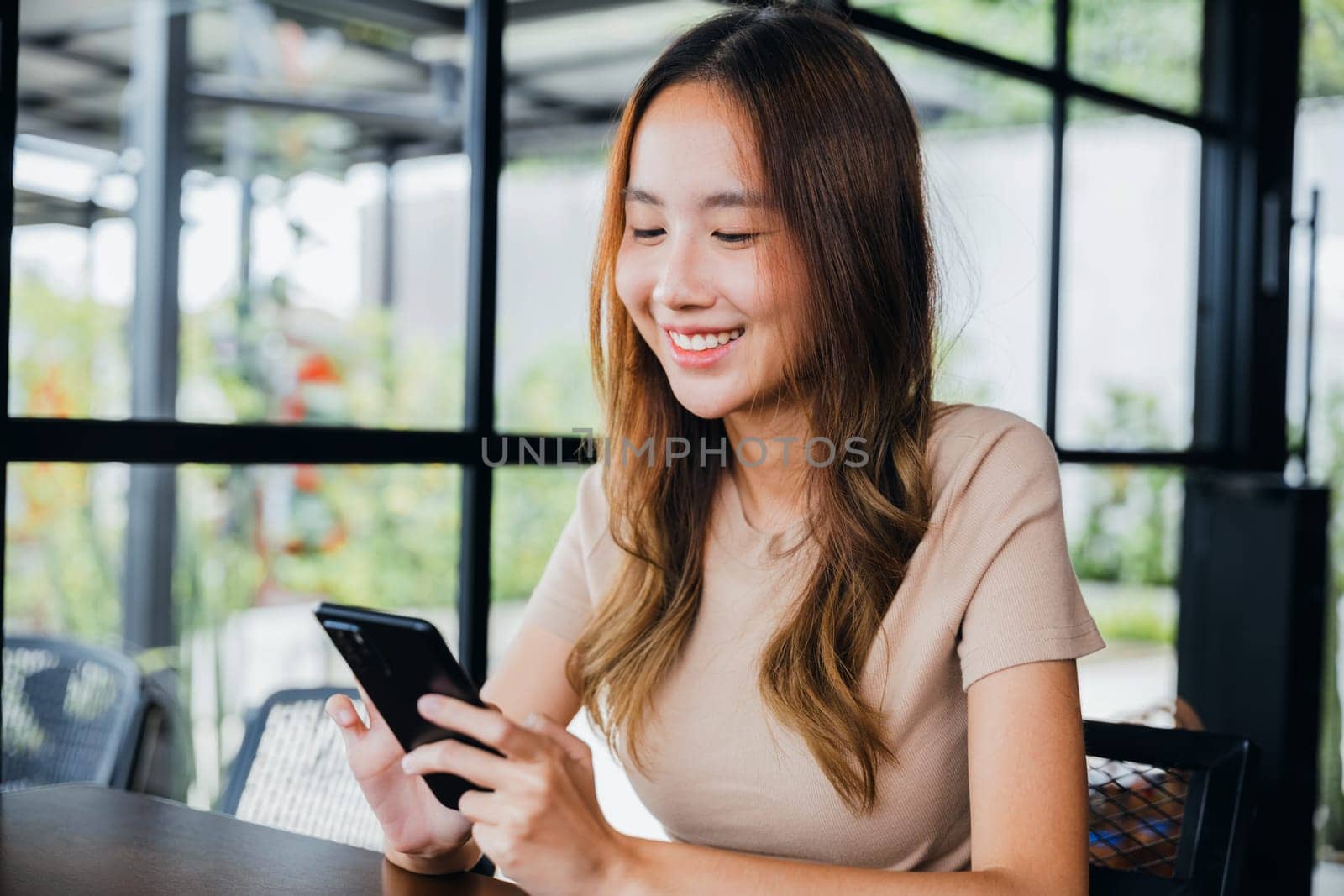 Beautiful Asian female has transfer money financial internet banking on mobile phone, young woman using smart phone for shopping online at cafe coffee shop near windows in the morning