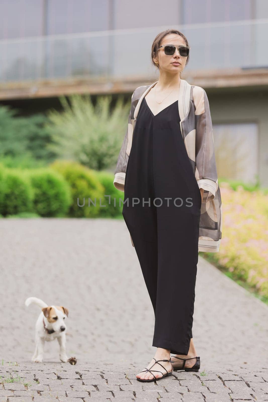 Beautiful young brunette woman, wearing black jumpsuit posing outdoors by sarymsakov