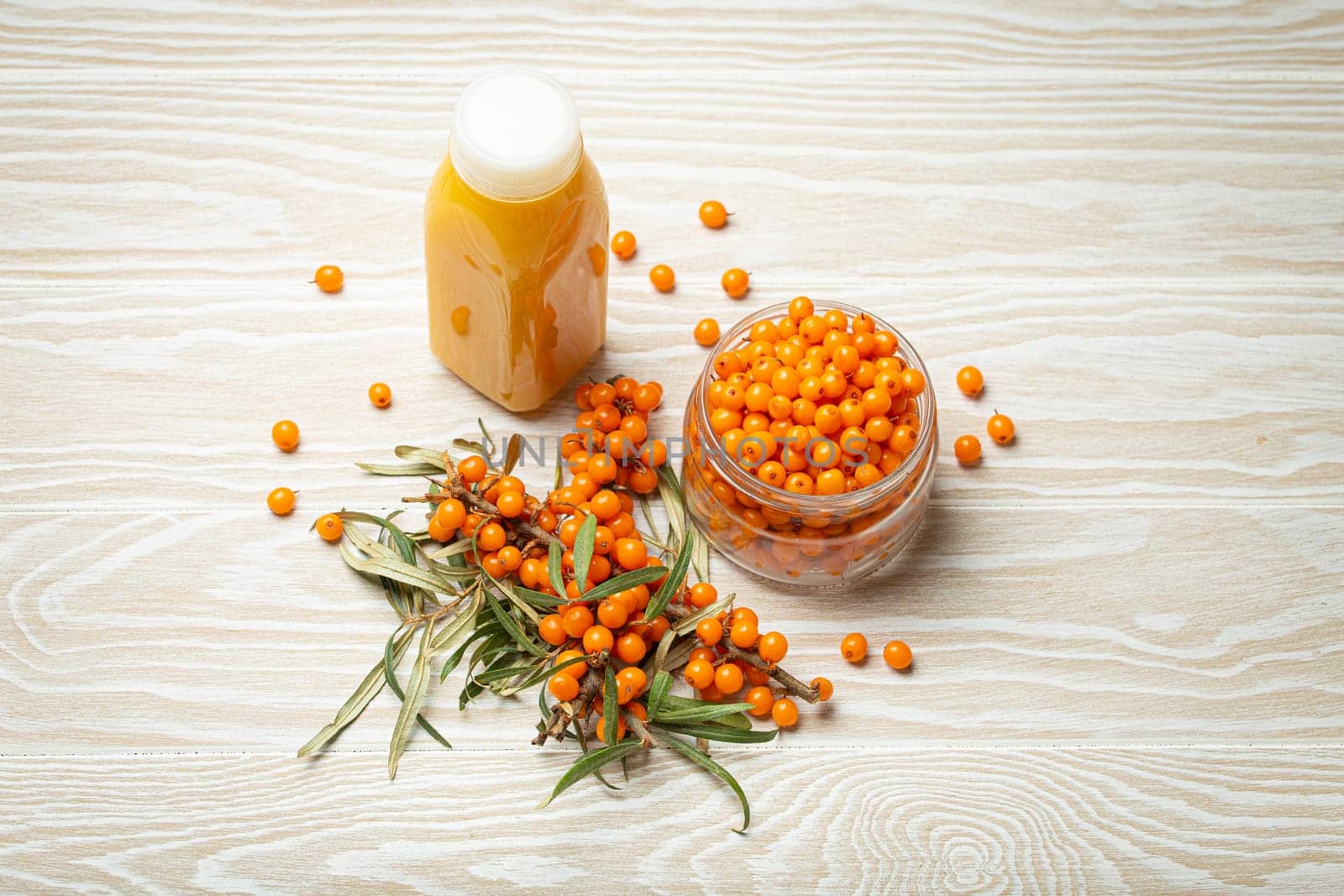 Sea buckthorn healthy drink in bottle, ripe berries in glass jar and branches with leaves top view on white wooden rustic background, great for skin, heart, vessels and immune system. by its_al_dente