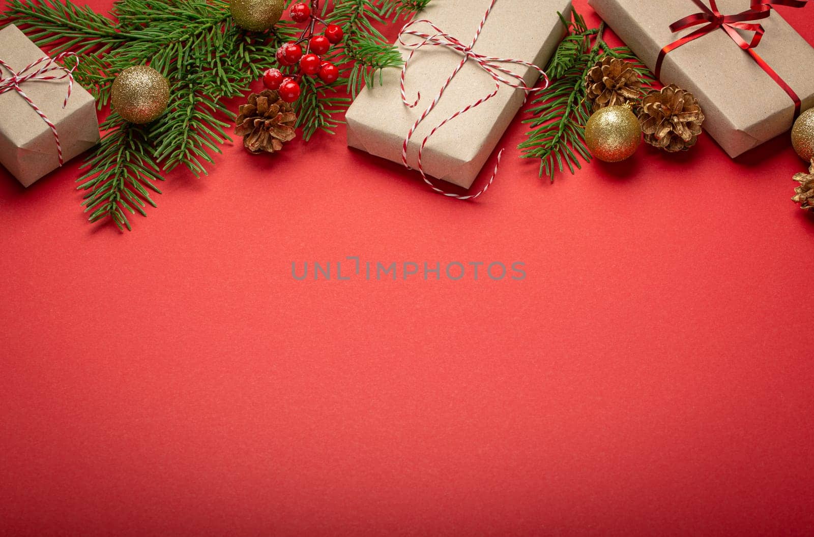 Christmas or New Year celebration red paper festive background with decoration fir tree, wrapped present boxes, cones, berries, sparkly red balls. Space for text..