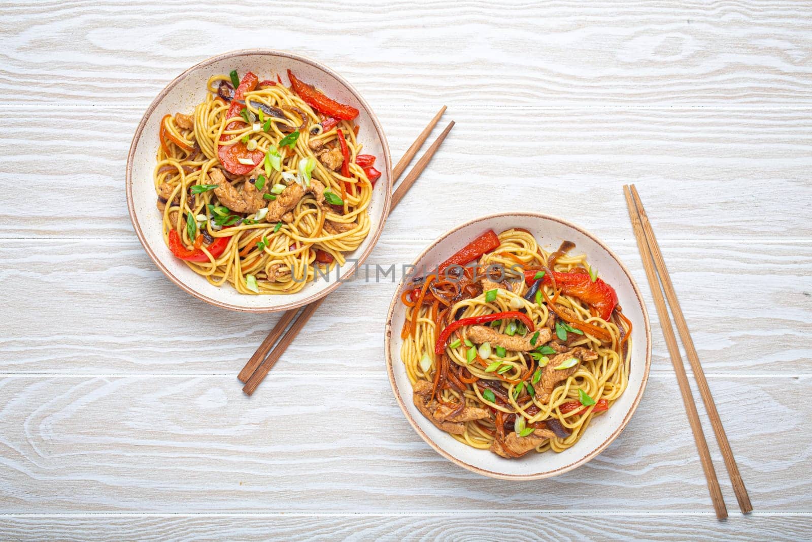 Two bowls with Chow Mein or Lo Mein, traditional Chinese stir fry noodles with meat and vegetables, served with chopsticks top view on rustic white wooden background table by its_al_dente