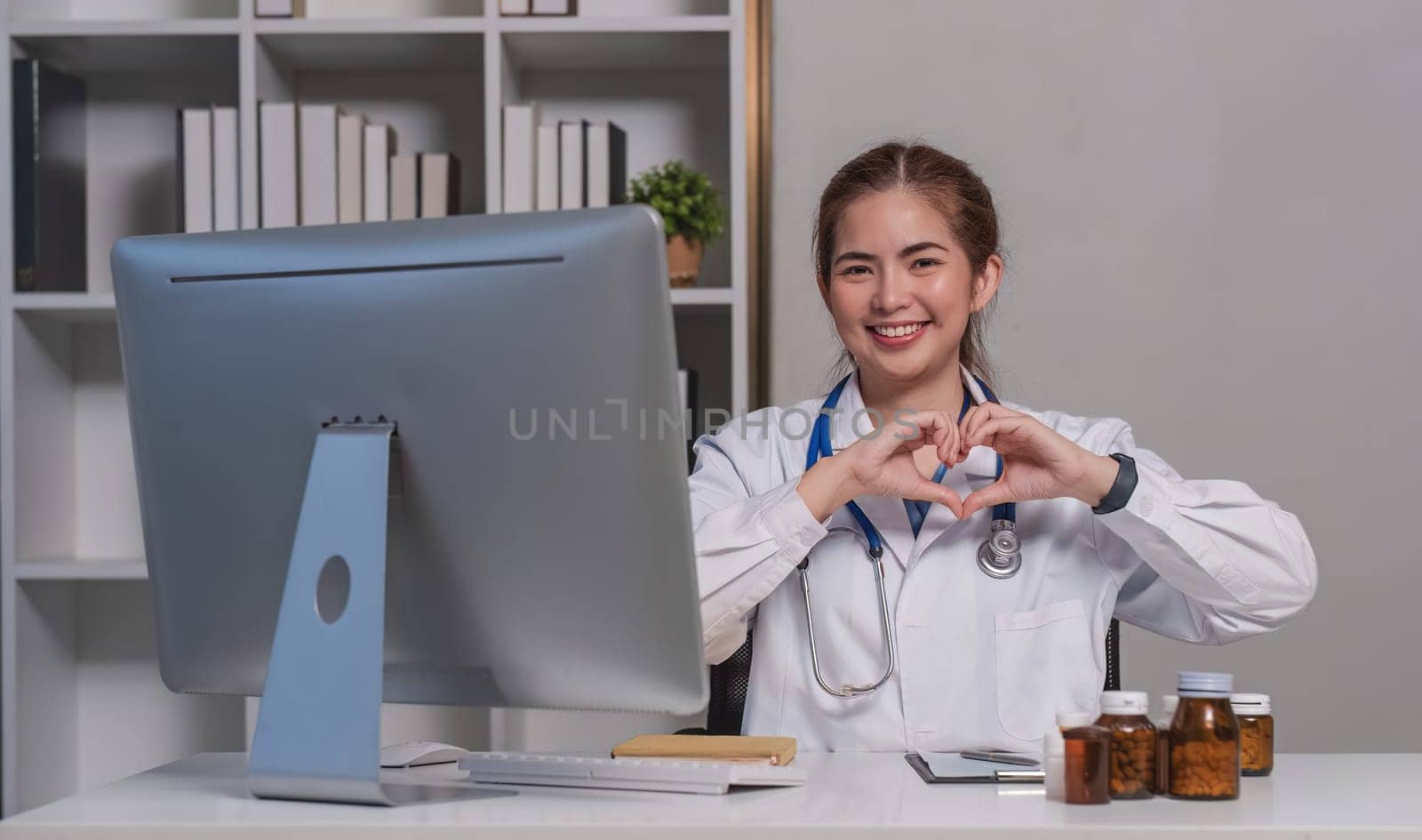 Beautiful asian woman wearing doctor uniform and stethoscope smiling in love doing heart symbol shape with hands. romantic concept. by wichayada