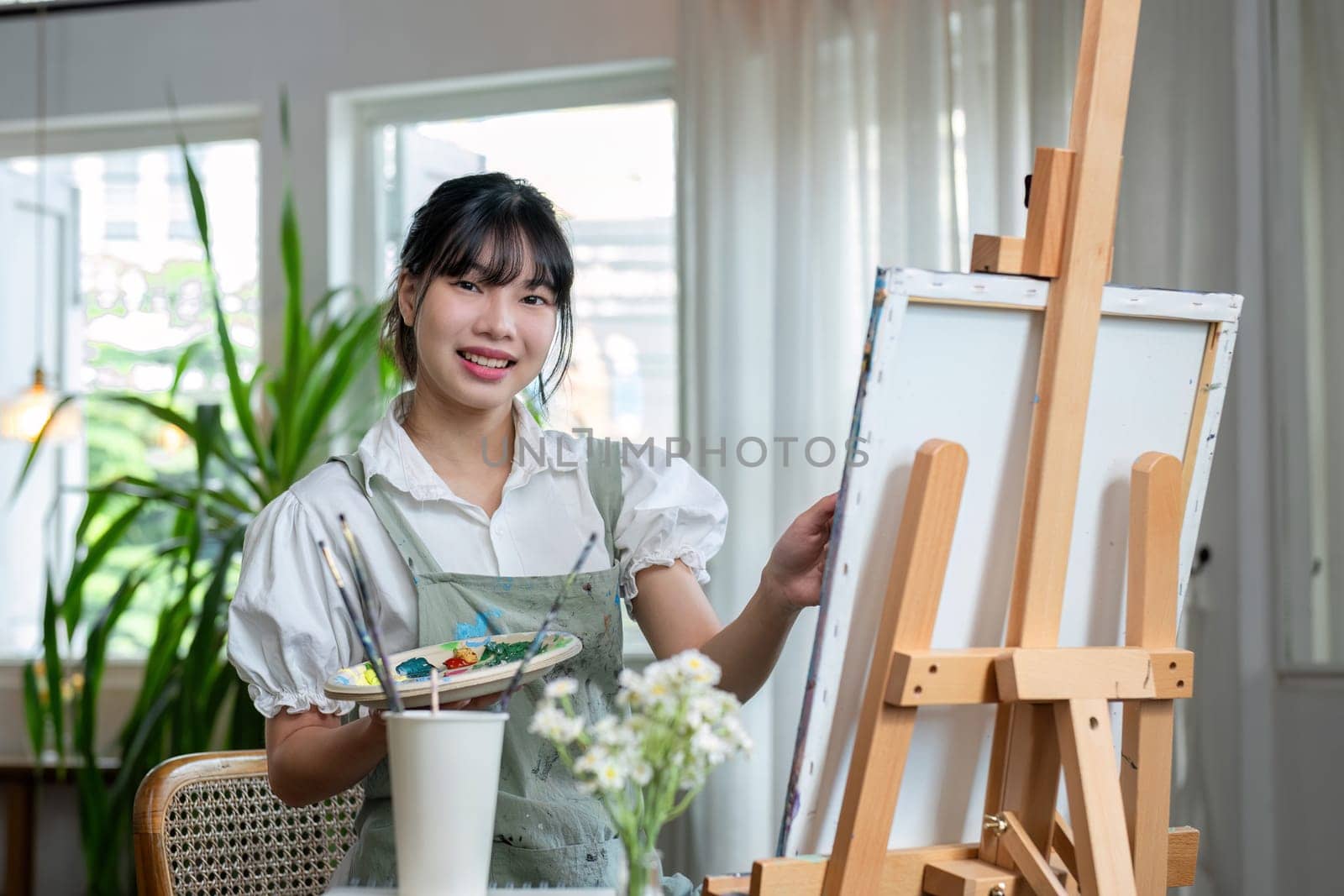 Young female artist works on abstract acrylic painting on canvas in art painting studio. by wichayada