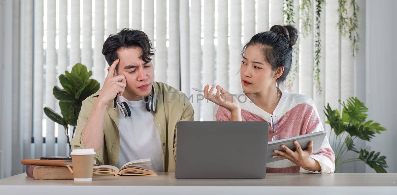 Two confused and thoughtful young Asian college friends are looking at a laptop screen with a serious face and don't understand an online lesson while studying together. by wichayada