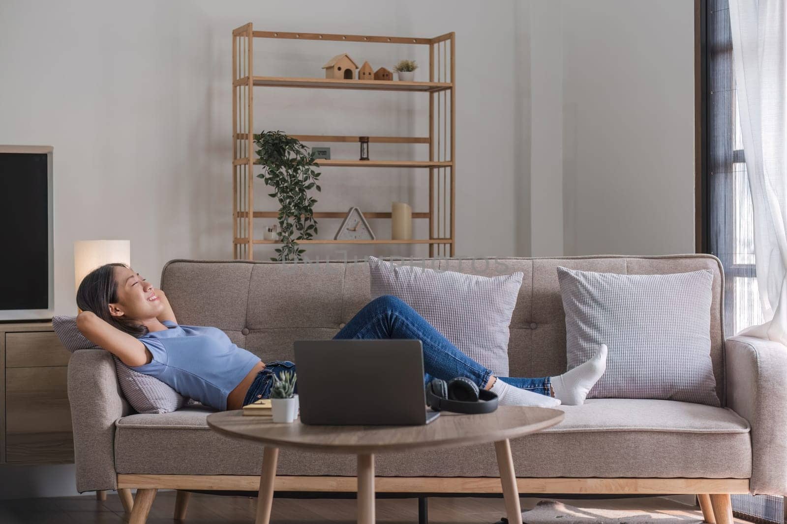 Woman listening music in headphones while lying on sofa in room.