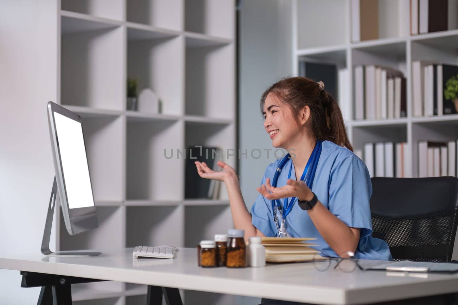 Beautiful Asian doctor smiling using laptop computer explaining detailed medical information online at hospital health medical concept. by wichayada