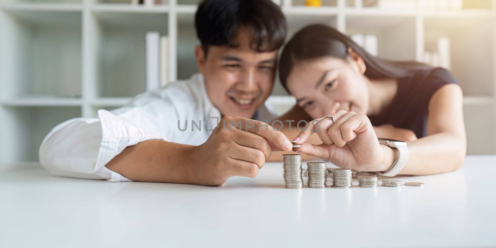 Happy Young Couple sitting with stacks of golden coins over table at home by itchaznong