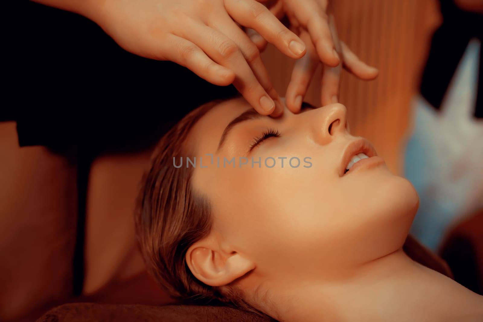 Caucasian woman enjoying relaxing anti-stress head massage and pampering facial beauty skin recreation leisure in warm candle lighting ambient salon spa in luxury resort or hotel. Quiescent