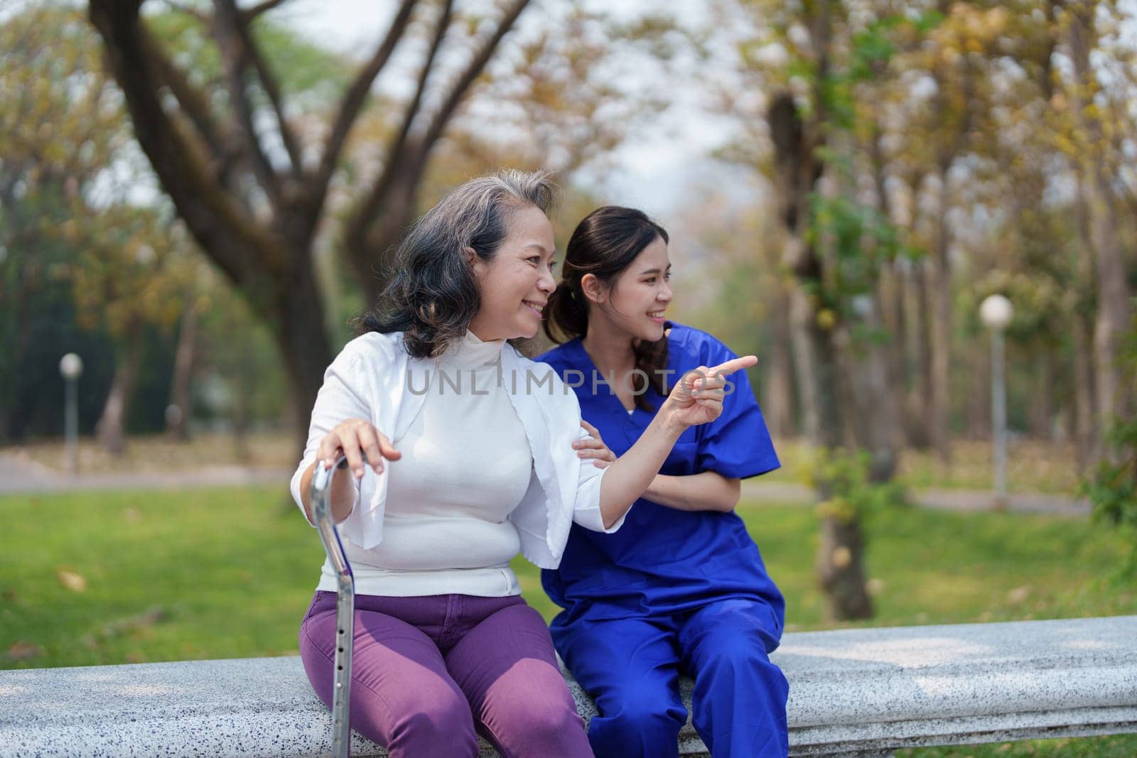 Patient care, female care, young Asian women are taking care of the elderly, providing crutches and walking for patients, and exercising their legs and knees in the park parks. by Manastrong