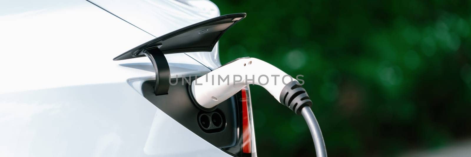 Closeup EV charger plug handle attached to electric vehicle port. Synchronos by biancoblue