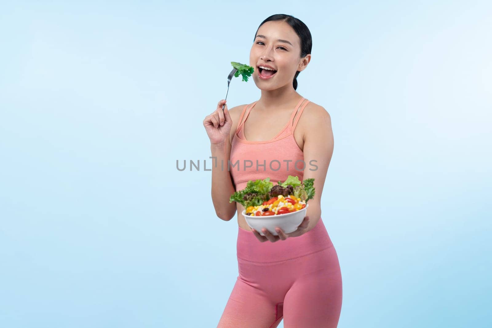 Young sporty Asian woman in sportswear holding salad bowl fill with vibrant of fruit and vegetable. Natural youthful and fit body lifestyle with balance nutrition on isolated background. Vigorous