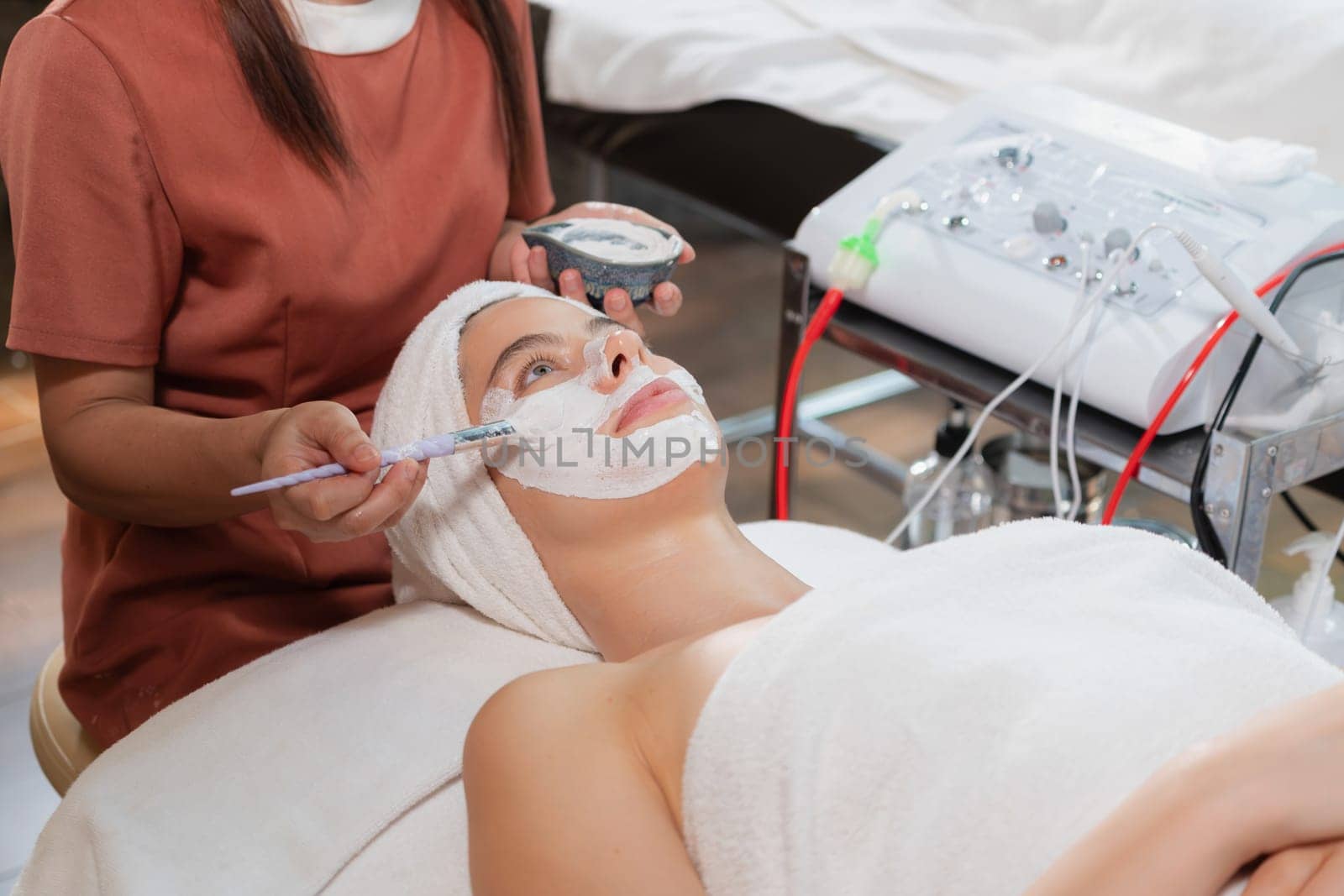 Beautiful young women lie on spa bed while having facial massage from professional doctor. Attractive female with beautiful skin surrounded by electric facial machine. Tranquility.