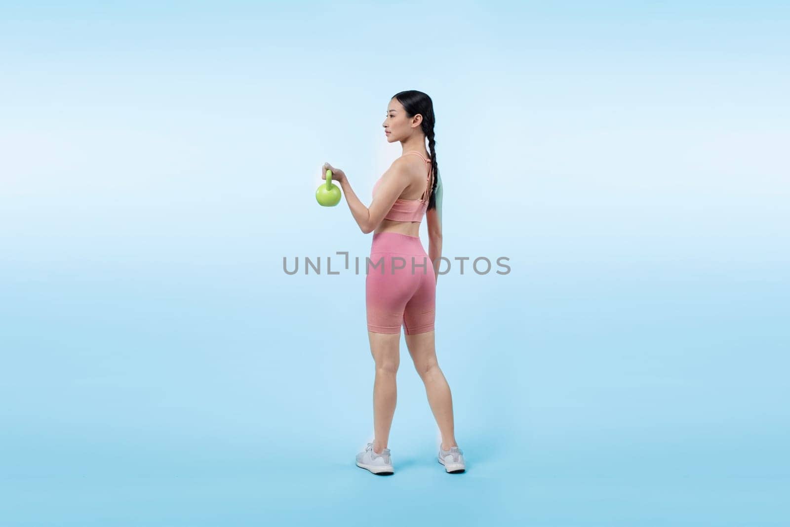 Vigorous energetic woman doing kettlebell weight lifting exercise on isolated background. Young athletic asian woman strength and endurance training session as body workout routine.