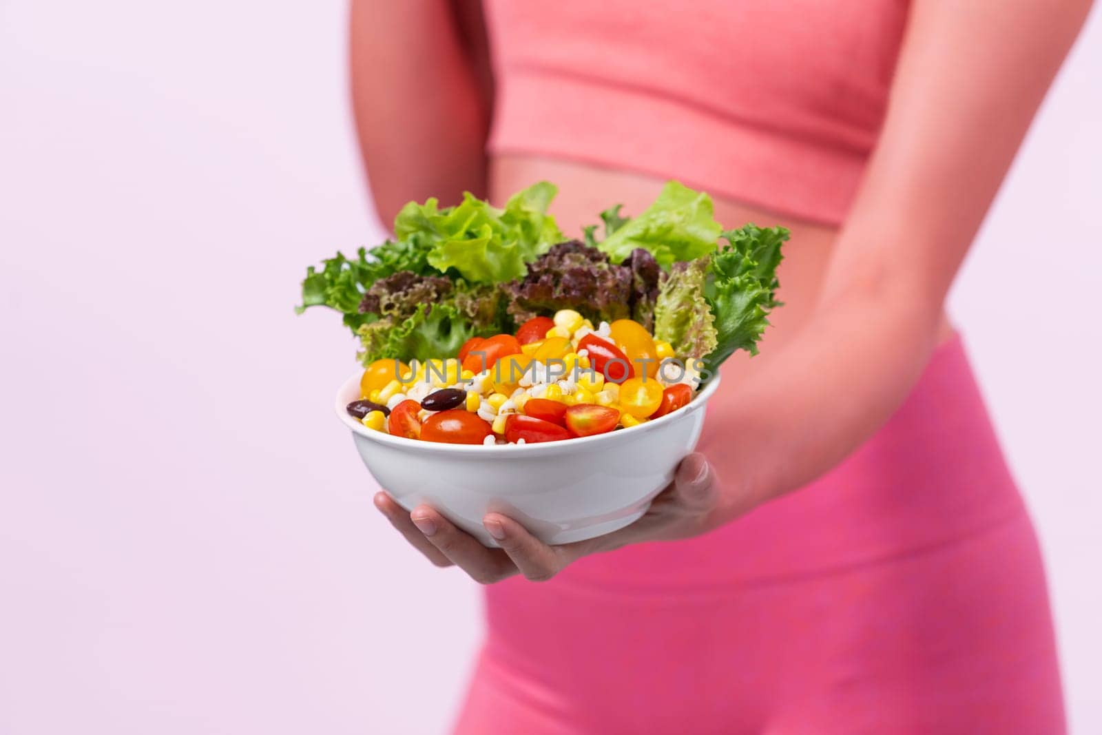 Young sporty Asian woman in sportswear holding salad bowl fill with vibrant of fruit and vegetable. Natural youthful and fit body lifestyle with balance nutrition on isolated background. Vigorous