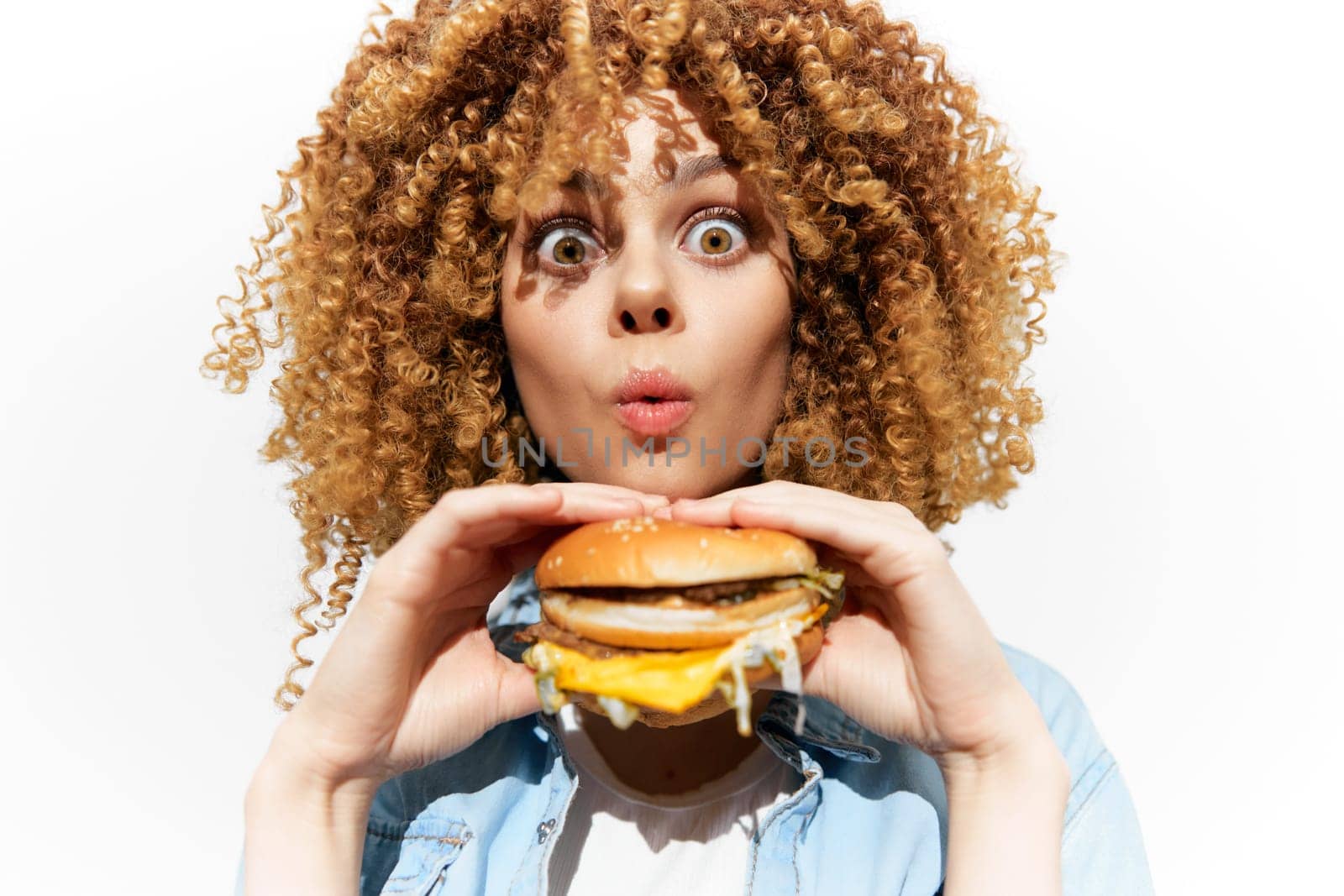 A cheerful young woman with curly hair expresses excitement while holding a cheeseburger This vibrant image highlights food enjoyment, ideal for food blogs and advertisements