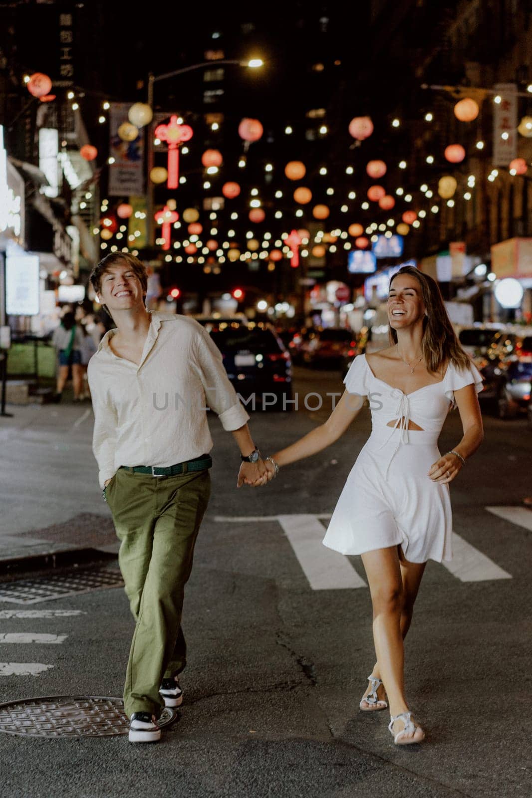 A charming couple leisurely strolls through a bustling city street, which is beautifully adorned with vibrant lanterns