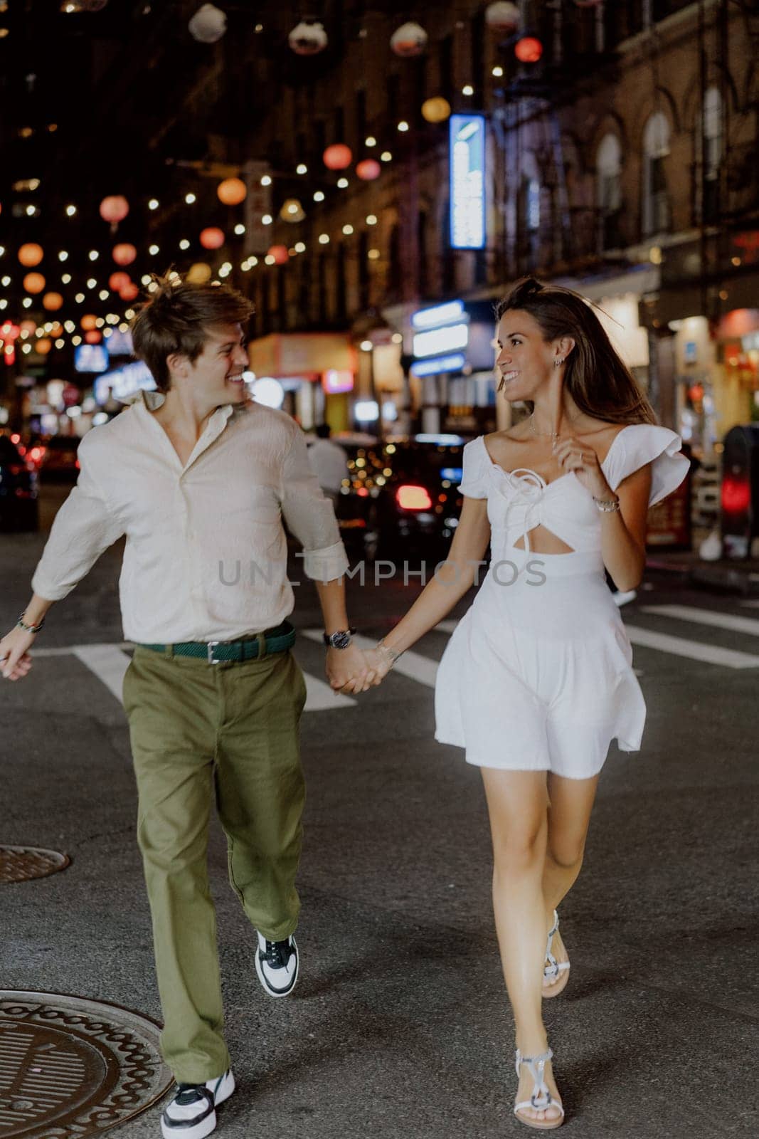 A charming couple leisurely strolls through a bustling city street, which is beautifully adorned with vibrant lanterns