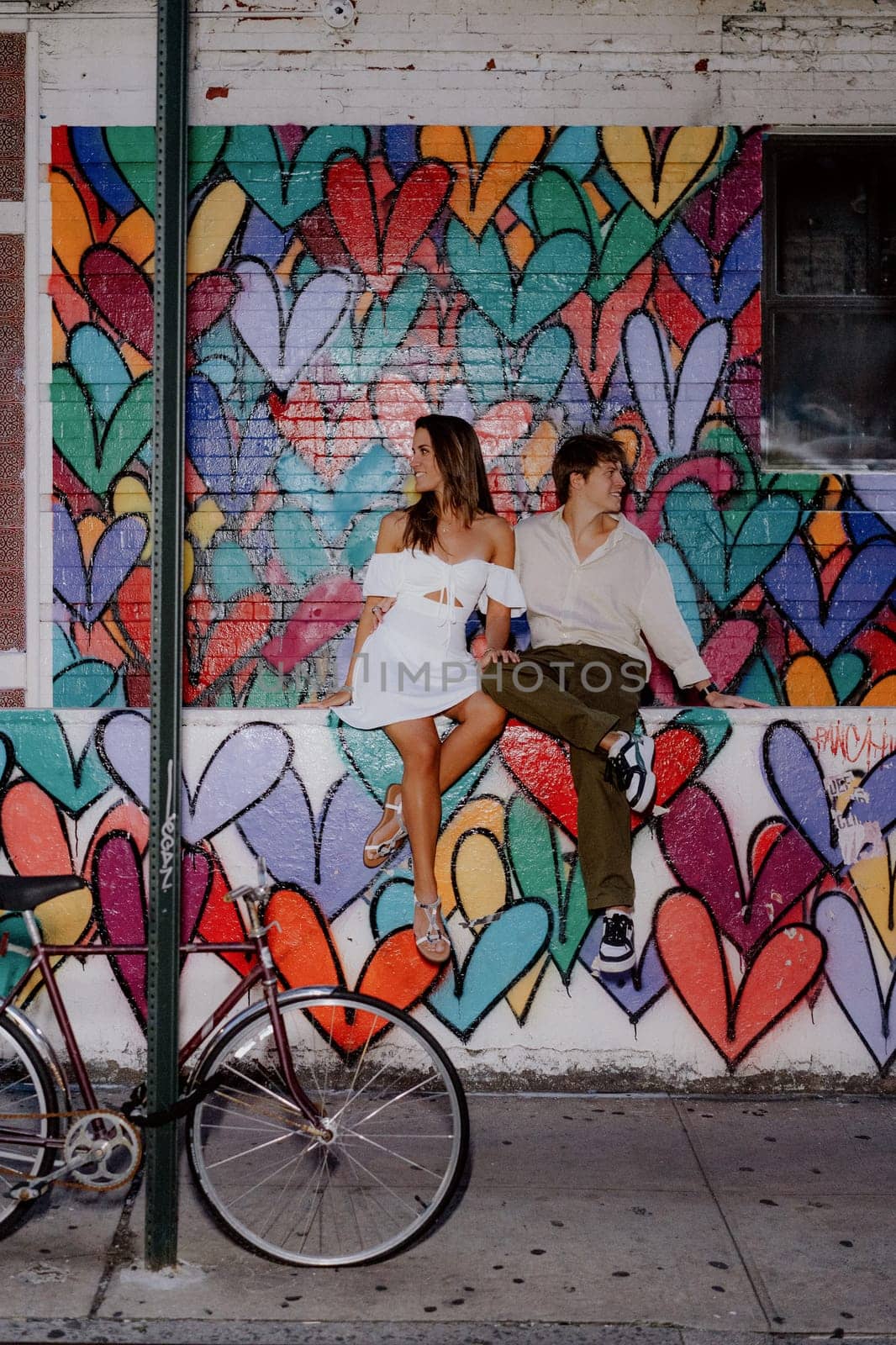 A couple kisses in front of a vibrant heart mural, symbolizing their love in a lively urban setting