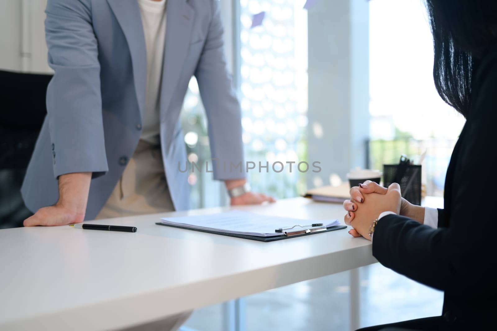 Cropped shot female candidate sitting with clasped hands at desk during job interview.