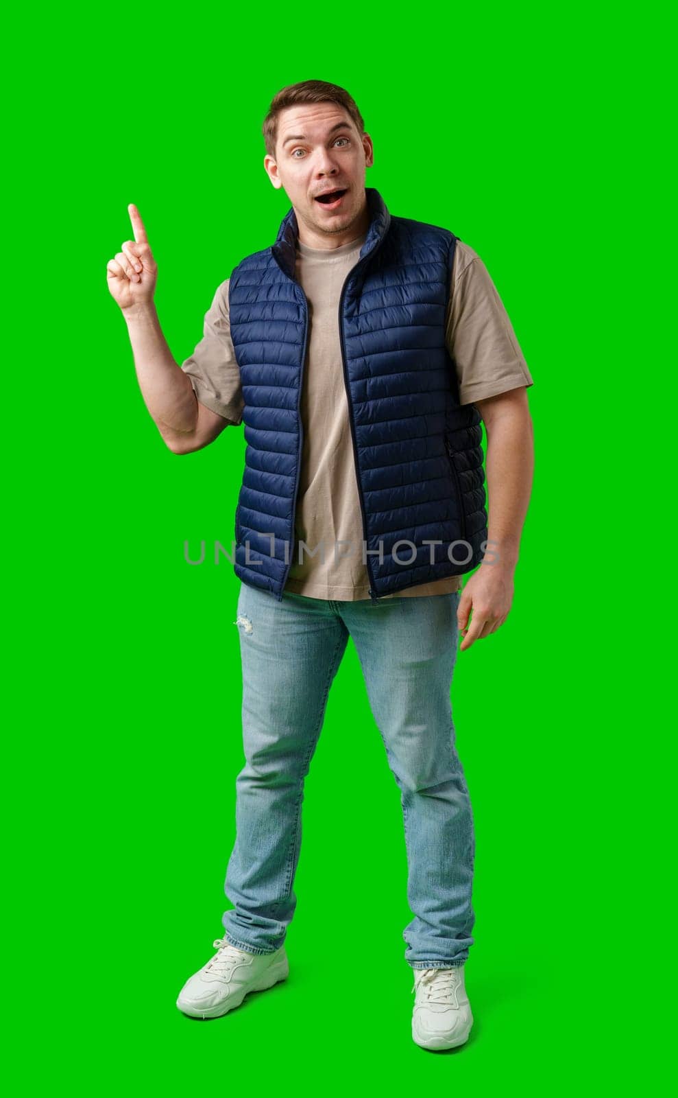 Man in a navy vest gestures enthusiastically toward a green screen in studio