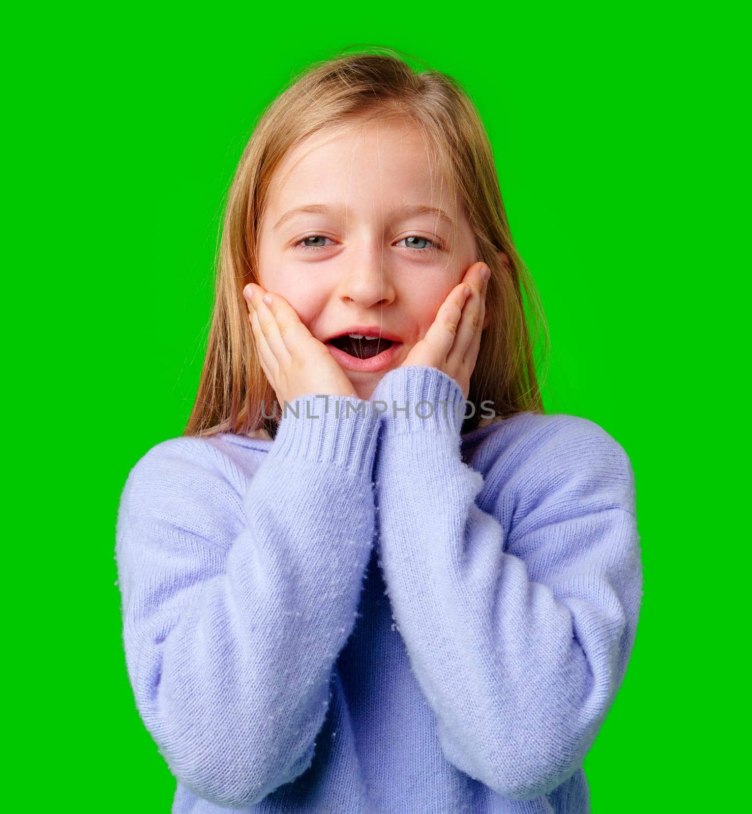 A young girl expresses surprise while smiling, with bright green background and cozy sweater