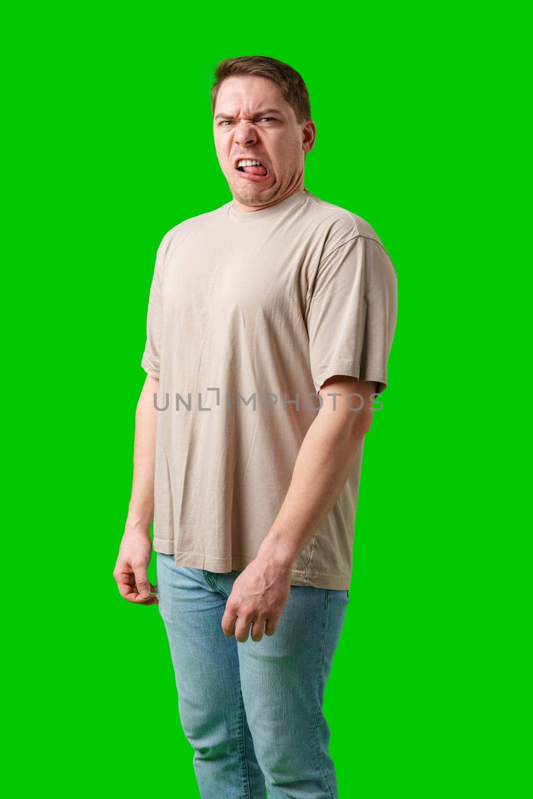 Young man making a disgusted expression while standing against a bright green background in studio