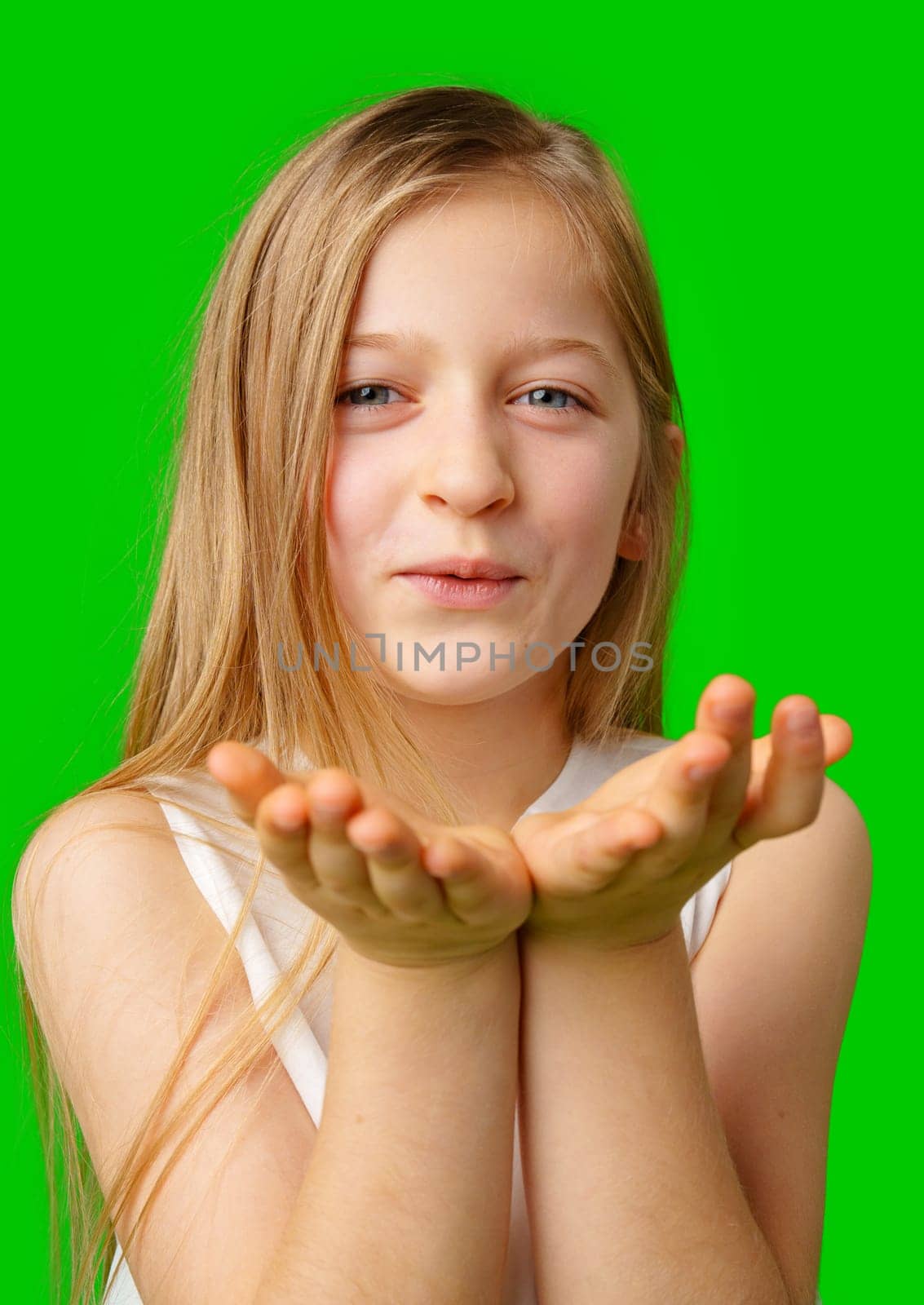 A young girl playfully blowing a kiss against a vibrant green background in studio
