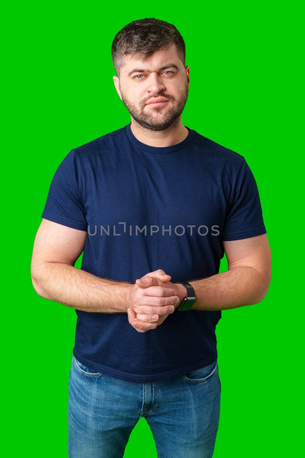 Man standing with a thoughtful expression in a casual outfit against a green background in studio