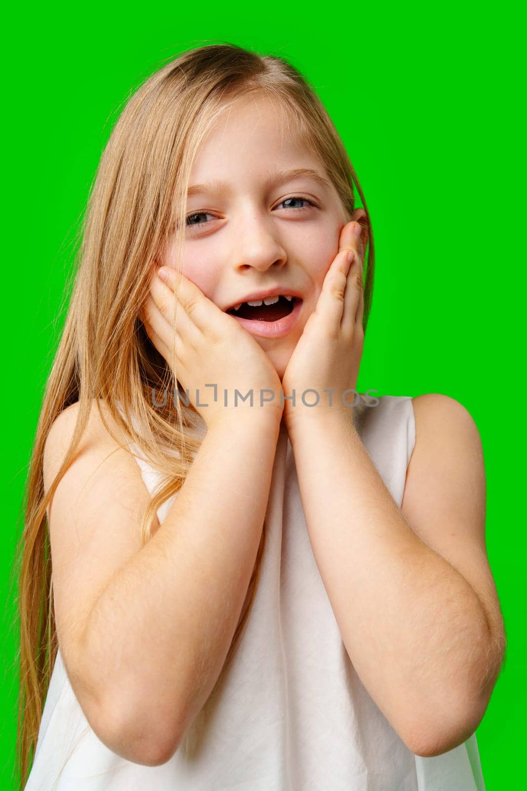 Young girl in a white dress surprised against a bright green background in studio