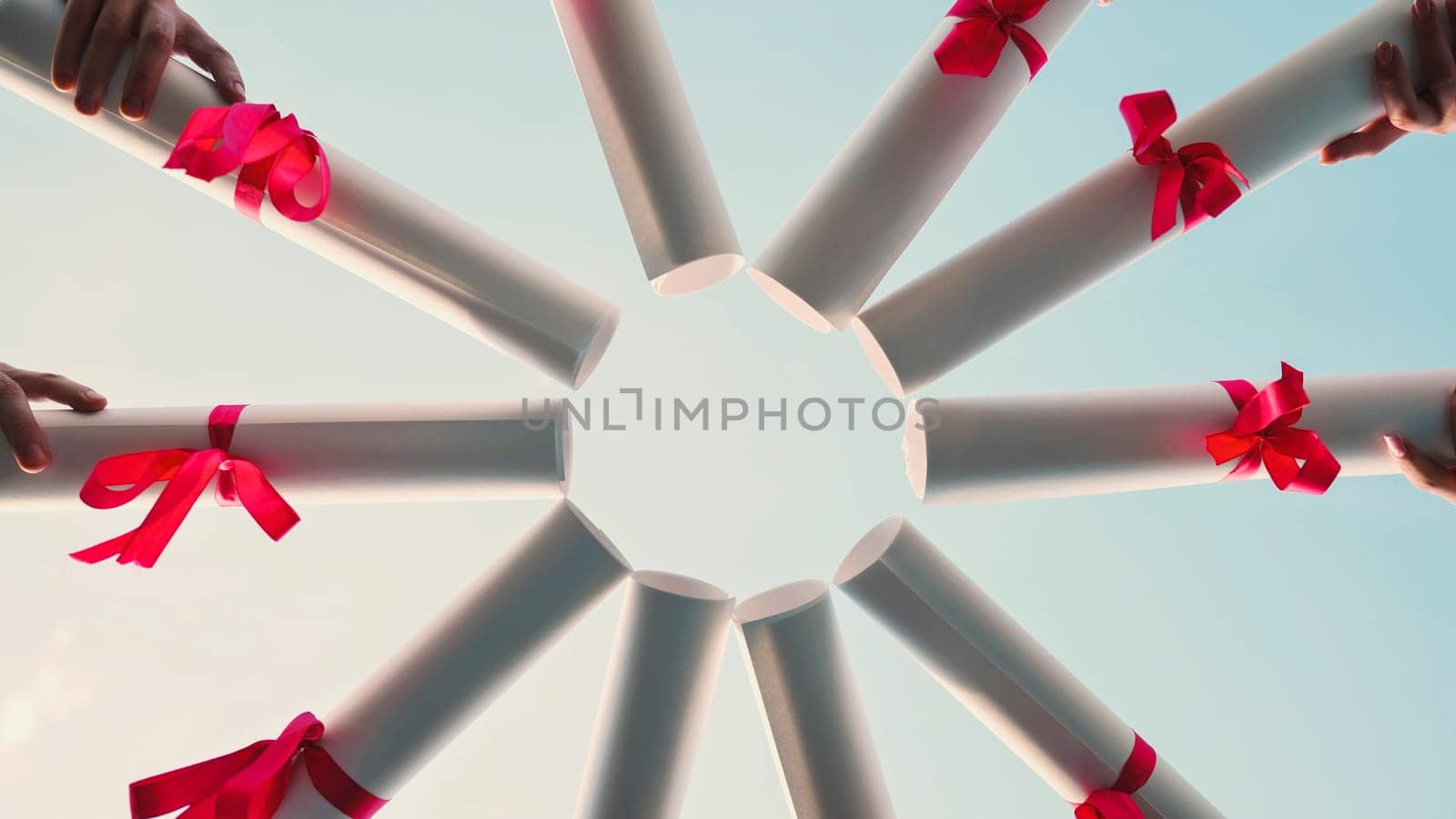Group of students celebrating their graduation by joining their diplomas, forming a circle against a clear blue sky