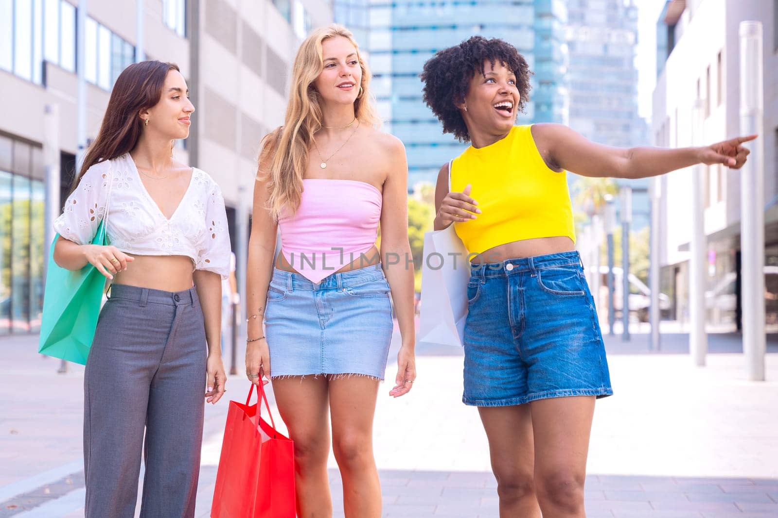 Three young women enjoying a sunny day, carrying shopping bags and smiling as they walk in an urban environment. Perfect for concepts like friendship, shopping, fashion, and lifestyle.