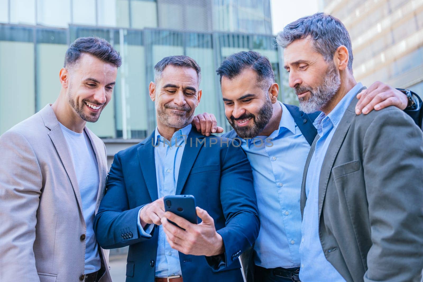 A group of confident businessmen standing outdoors in a modern urban setting. They are smiling and looking at a smartphone, symbolizing teamwork, technology, and connection.