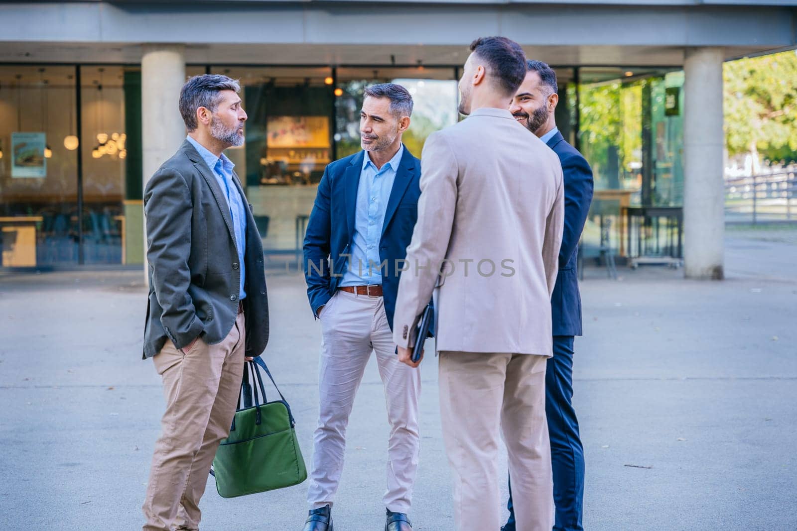Group of four businessmen in formal and smart casual attire discussing outdoors in a modern urban setting, demonstrating teamwork and collaboration.